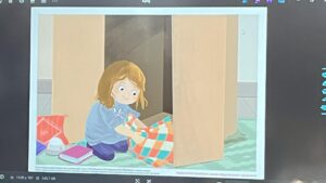 Na ilustracji widać dziewczynkę o rudawych włosach, która klęczy na podłodze przed otwartą szafą z kartonu lub drewnianą szafką. Ubrana jest w niebieską bluzę i fioletowe spodnie. W rękach trzyma kolorowy kocyk w kratkę z pomarańczowych, turkusowych i białych pól, który układa lub wyciąga z wnętrza szafy. Obok niej leżą różowe kapcie, książka i czerwony plecak z białym wzorem. Podłoga pokryta jest zielonym dywanem o falistym wzorze. Dziewczynka wygląda na skupioną i spokojną, jakby przygotowywała coś w tajemnicy lub porządkowała swoje rzeczy. Cała scena jest ciepła i przytulna, utrzymana w pastelowych barwach.