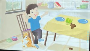 Na ilustracji widać chłopca siedzącego na krześle przy stole w kuchni. Ma na sobie niebieską koszulkę, ciemne spodnie i skarpetki w paski. Obok niego, przy nodze krzesła, stoi pomarańczowo-biały kot z uniesionym ogonem.

Na stole przykrytym żółtym obrusem widać dwa niebieskie talerze i zielony kubek, który się przewrócił, rozlewając napój – prawdopodobnie kakao lub czekoladę. Część napoju spadła również na podłogę. Chłopiec ma uniesione ręce i zaskoczoną minę, jakby właśnie zauważył, co się stało.

W tle widać kuchenny blat z garnkami, owocami i zlewem, a przez okno wpada światło dzienne, co nadaje scenie ciepły, domowy charakter.
