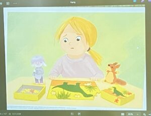 Na tym obrazku widzę ilustrację przedstawiającą dziecko bawiące się zabawkami:

Główna postać:

Dziewczynka z jasnymi, żółtymi włosami spiętymi w kucyk
Ubrana w jasnoróżową/beżową bluzę
Ma duże, niebieskie oczy i delikatny, zamyślony wyraz twarzy
Patrzy w dół na zabawki przed sobą
Zabawki na stole:

Trzy żółte pudełka/tacki z różnymi elementami:
Pudełko po lewej z małymi elementami/klockami
Środkowe pudełko z zieloną scenką przedstawiającą łąkę z białymi kwiatkami (stokrotkami) i trawą
Pudełko po prawej z kwiatkami i zielonymi elementami
Figurka chłopca (po lewej stronie) - niebieska postać stojąca na pudełku
Figurka królika/zająca (po prawej stronie) - pomarańczowa postać
Tło i atmosfera:

Jasne, pastelowe tło w odcieniach zieleni i żółci
Delikatny, akwarelowy styl ilustracji
Spokojna, kontemplacyjna atmosfera
Ilustracja typowa dla książek dla dzieci
Scena przedstawia moment zabawy lub nauki, gdzie dziecko skupia się na układaniu lub obserwowaniu swoich zabawek.