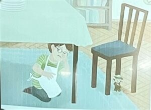 Na obrazku widzę ilustrację z książki, wykonaną w delikatnym, akwarelowym stylu:

Główny motyw:

Dziecko w okularach i zielonej koszulce w paski, siedzące/chowające się pod stołem
Dziecko trzyma w rękach zieloną książkę i ma nieco zmartwioną lub zamyśloną minę
Widoczne są nogi dziecka w ciemnych butach/skarpetkach
Otoczenie:

Duży stół z jasnoniebieskim obrusem
Drewniane krzesło z pionowymi szczeblami w oparciu i niebieskim siedziskiem
Pod krzesłem widać małą zabawkową figurkę (prawdopodobnie misia lub inną postać)
W tle widoczna drewniana podłoga z wzorem parkietu
Delikatnie zarysowane meble w tle (regał lub szafka)
Atmosfera:
Ilustracja ma spokojny, intymny charakter. Przedstawia dziecko w swoim prywatnym "świecie" pod stołem - klasyczne dziecięce miejsce do zabawy lub ukrycia się. Pastelowe, miętowo-błękitne tony i akwarelowa technika nadają scenie delikatny, nostalgiczny nastrój. Może to być moment czytania w ukryciu lub chwila samotności i zadumy.