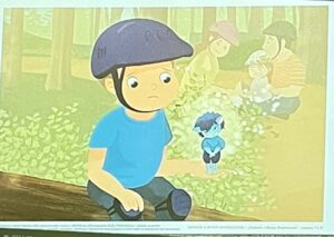 Zdjęcie przedstawia ekran komputera z edukacyjną ilustracją dla dzieci - chłopiec siedzący na pniu drzewa, obserwujący inne dzieci bawiące się w tle.

Ilustracja na ekranie (centrum):

Styl graficzny:

Ilustracja dla dzieci - miękki, akwarelowy styl
Pastelowe, ciepłe kolory - żółty, zielony, niebieski
Delikatne, rozmyte kontury - artystyczny efekt
Styl książki obrazkowej - edukacyjna estetyka
Spokojny, refleksyjny nastrój
Główna postać - chłopiec (lewo, pierwszy plan):

Wygląd:

Duża, okrągła głowa - proporcje ilustracji dziecięcej
Żółta/beżowa twarz - prosta, płaska
Duże, okrągłe oczy - patrzą w dal
Mały nosek - kropka lub kreska
Poważny/zamyślony wyraz twarzy - nie uśmiecha się
Czarna linia jako usta - neutralny lub lekko smutny
Ubranie:

Niebieska koszulka (jasny, turkusowy niebieski)
Ciemnoszare/granatowe spodnie
Szare buty
Duży, szary hełm na głowie
Ochronny hełm (rowerowy lub budowlany)
Okrągły, wypukły kształt
Ciemnoszary kolor
Pozycja:

Siedzi na pniu drzewa (brązowy, poziomy pień)
Nogi zwisają - swobodna pozycja
Ręce na kolanach lub obok ciała
Patrzy w stronę innych dzieci (prawo)
Postawa obserwatora - nie uczestniczy w zabawie
Emocje:

Zamyślony - patrzy w dal
Samotny? - siedzi z boku
Obserwujący - patrzy na innych
Spokojny - nie wykazuje silnych emocji
Może smutny lub nieśmiały - nie bawi się z innymi
Dzieci w tle (prawo, centrum):

Grupa dzieci (około 3-4 postaci):

Rozmyte sylwetki - w tle, mniej wyraźne
Różne kolory ubrań:
Różowy/beżowy (jedno dziecko)
Żółty w paski (drugie dziecko)
Inne kolory (niewyraźne)
Hełmy na głowach - różne kolory (różowy, brązowy)
Aktywne postacie - w ruchu, bawią się
Skupione na zabawie - nie patrzą na główną postać
Dziecko w centrum (między główną postacią a grupą):

Małe dziecko - mniejsza sylwetka
Niebieskie ubranie (ciemny niebieski)
Hełm na głowie
Stoi lub idzie - w ruchu
Może biegnie w stronę grupy
Otoczenie - park/las (tło):

Rośliny (centrum, dół):

Gęste, zielone krzewy lub niskie rośliny
Jasna, żółtozielona zieleń - słoneczne światło
Bujne zarośla - naturalne środowisko
Rozmyte, malarskie - efekt akwareli
Drzewa (tło, góra):

Wysokie pnie drzew (brązowe, pionowe linie)
Zielone korony - liście w tle
Las lub park - naturalne otoczenie
Żółtozielone światło - filtrowane przez liście
Ciepła, słoneczna atmosfera
Pień drzewa (lewo, dół):

Brązowy, poziomy pień - ścięte lub powalone drzewo
Gruba, solidna powierzchnia
Siedzisko dla chłopca
Naturalne, drewniane - tekstura drewna
Kolorystyka:

Dominujący żółtozielony - słoneczny, ciepły
Niebieski (ubrania) - chłodny akcent
Szary (hełm) - neutralny
Brązowy (drzewa, pień) - naturalne elementy
Pastelowe, stonowane - spokojny nastrój
Rozmyte przejścia - akwarelowy efekt
Interfejs komputera (widoczny):

Dolny pasek (dół ekranu):

Pasek narzędzi - ikony, przyciski
Niewyraźne elementy - standardowy interfejs przeglądarki lub programu
Charakterystyka:

Temat ilustracji: Samotność, nieśmiałość lub wykluczenie - dziecko obserwujące zabawę innych

Możliwe interpretacje:

1. Nieśmiałość:

Chłopiec chce się bawić, ale nie wie jak dołączyć
Obserwuje innych, zbierając odwagę
Czeka na zaproszenie lub odpowiedni moment
2. Samotność:

Chłopiec czuje się samotny - inni się bawią bez niego
Wykluczony z zabawy
Smutny lub zamyślony
3. Obserwacja:

Chłopiec po prostu obserwuje - nie musi być smutny
Spokojny moment - odpoczynek
Refleksja - myśli o czymś
4. Przygotowanie do dołączenia:

Chłopiec zaraz dołączy do zabawy
Moment przejściowy - między samotnością a zabawą
Zbiera odwagę lub planuje
Cel edukacyjny:

Tematy do omówienia z dziećmi:

Emocje - jak się czuje chłopiec?
Samotność - co zrobić, gdy czujesz się samotny?
Nieśmiałość - jak dołączyć do zabawy?
Empatia - jak pomóc komuś, kto jest sam?
Włączanie innych - zapraszanie do zabawy
Przyjaźń - jak nawiązywać relacje?
Pytania dla dzieci:

"Jak myślisz, co czuje chłopiec?"
"Dlaczego siedzi sam?"
"Co mogą zrobić inne dzieci?"
"Co chłopiec może zrobić, żeby dołączyć?"
"Czy kiedyś czułeś się tak jak on?"
Wartości edukacyjne:

Rozpoznawanie emocji - identyfikacja uczuć
Empatia - rozumienie innych
Umiejętności społeczne - jak dołączyć do grupy
Radzenie sobie z samotnością - strategie
Włączanie innych - bycie dobrym kolegą
Możliwe zastosowanie:

Lekcja o emocjach - rozpoznawanie uczuć
Warsztaty społeczne - umiejętności interpersonalne
Rozmowa o przyjaźni - jak być dobrym przyjacielem
Przeciwdziałanie wykluczeniu - włączanie wszystkich
Edukacja emocjonalna - radzenie sobie z trudnymi uczuciami
Kontekst narracyjny:

Możliwa historia:

Początek: Chłopiec przyszedł do parku
Problem: Inne dzieci już się bawią, on nie wie jak dołączyć
Konflikt wewnętrzny: Chce się bawić, ale boi się podejść
Rozwiązanie (niewidoczne): Może dołączy? Może ktoś go zaprosi?
Przekaz dla dzieci:

Dla dziecka, które czuje się jak chłopiec:

Nie jesteś sam - inni też czasem tak się czują
Możesz poprosić o dołączenie - "Czy mogę się z wami bawić?"
To normalne - wszyscy czasem czują się nieśmiało
Odwaga - spróbuj podejść
Dla dzieci, które widzą kogoś samotnego:

Zauważ - ktoś może potrzebować zaproszenia
Zaproś - "Chodź, pobaw się z nami!"
Bądź miły - włączaj innych do zabawy
Empatia - pomyśl, jak by się czuł
Aspekt psychologiczny:

Normalizacja uczuć - samotność to normalne uczucie
Strategie radzenia sobie - co mogę zrobić?
Budowanie pewności siebie - mogę dołączyć
Rozwój społeczny - nauka interakcji
Styl artystyczny:

Miękki, akwarelowy - nie przeraża, uspokaja
Rozmyte tło - skupienie na głównej postaci
Ciepłe kolory - mimo smutnego tematu, atmosfera nie jest mroczna
Prosty design - czytelny dla małych dzieci (4-8 lat)
Wzruszająca, edukacyjna ilustracja poruszająca ważny temat społeczny - samotność, nieśmiałość i włączanie innych. Wyraz twarzy chłopca i jego odizolowana pozycja jasno komunikują emocje, co czyni ilustrację doskonałym narzędziem do rozmów z dziećmi o:

Uczuciach - jak rozpoznać i nazwać emocje
Empatii - jak rozumieć innych
Umiejętnościach społecznych - jak nawiązywać kontakty
Włączaniu innych - jak być dobrym kolegą
Miękki, artystyczny styl sprawia, że trudny temat jest przedstawiony w łagodny, przystępny sposób, odpowiedni dla małych dzieci. Ilustracja nie osądza, tylko pokazuje sytuację, pozwalając dzieciom samodzielnie zastanowić się nad rozwiązaniem.